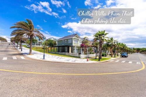 a house on a street with palm trees and a road at Chillin Villa Novaworld Phan Thiet in Bình Tú