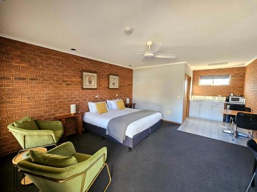 a bedroom with a bed and chairs and a brick wall at Bridge Motor Inn Tocumwal in Tocumwal