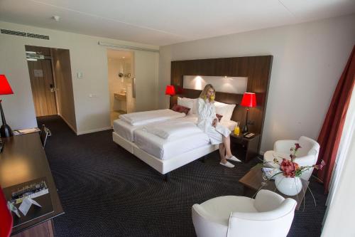 a woman sitting on a bed in a hotel room at Van der Valk Hotel Assen in Assen