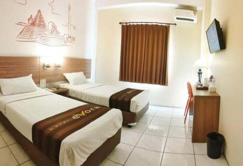 a hotel room with two beds and a desk at Evora Hotel in Surabaya