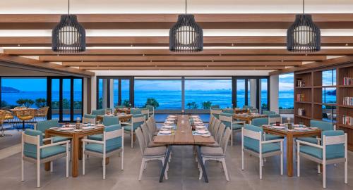Un comedor con mesas y sillas y ventanas. en Avani+ Barbarons Seychelles, en Grand'Anse
