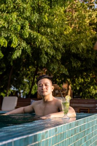 a man sitting in a swimming pool with a drink at Payana Kampot in Kampot