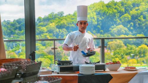 uno chef in piedi in cucina che tiene in mano una padella di Oak Ray Heritage Hotel a Kandy