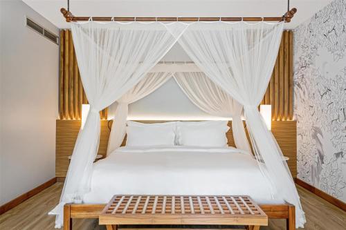 a bedroom with a canopy bed with a wooden table at Kempinski Seychelles Resort in Baie Lazare Mahé
