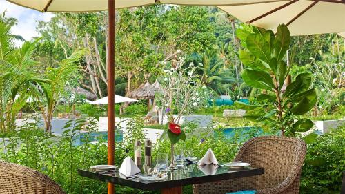 a table with chairs and an umbrella in a garden at Kempinski Seychelles Resort in Baie Lazare Mahé