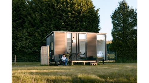 a woman sitting on a bench in front of a tiny house at Harrington's on the Terrace - Murchison by Tiny Away in Te Anau
