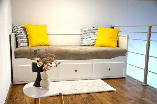 a bed with yellow pillows and a vase on a table at Loftas Smilga in Palanga