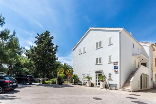 a white building with cars parked in a parking lot at Apartments Lavica Beach Dumičić in Podstrana