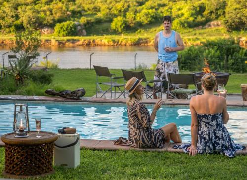 a man and two women sitting next to a swimming pool at Kambaku River Lodge in Malelane