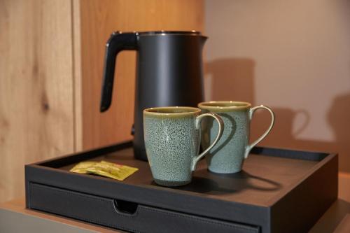 two cups sitting on a shelf with a coffee pot at Sporthotel Grafenwald 4 Sterne Superior in Daun