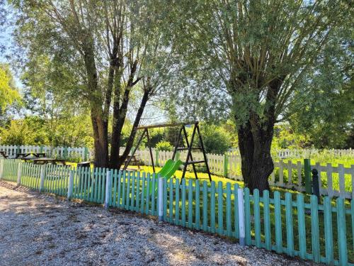 a blue fence with a playground in front of two trees at La Colline aux Fustes in Meurville