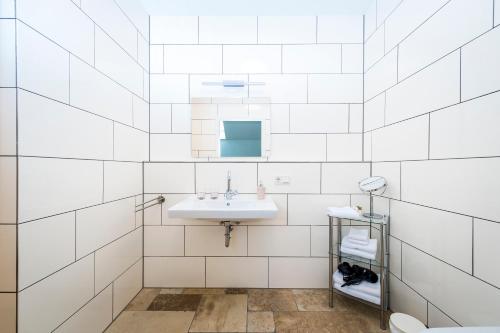 a white tiled bathroom with a sink and a mirror at Hofgut Dösterhof - Hotelzimmer in Wadern