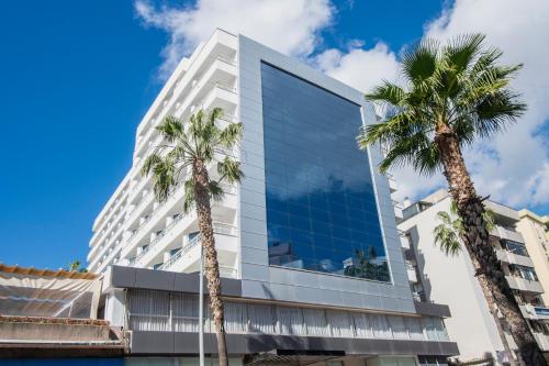 a tall white building with palm trees in front of it at Hotel Costa Málaga - Adults Recommended - by Pierre & Vacances in Torremolinos