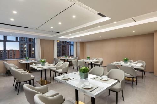 a restaurant with white tables and chairs and windows at Ramada by Wyndham Urumqi Midong in Ürümqi