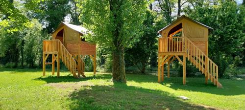 two wooden playhouses sitting next to a tree at Camping Onlycamp Les Adoubes - Albertville in Albertville