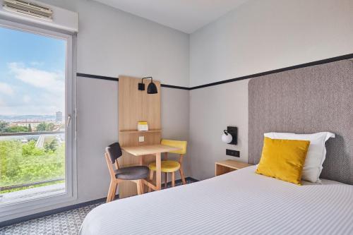a hotel room with a bed and a desk and a window at Appart'hôtel Odalys City - Bioparc Lyon Est in Lyon