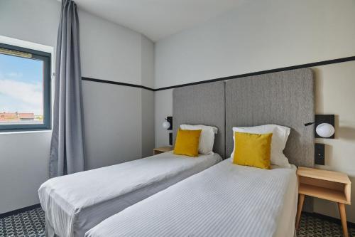 two beds in a hotel room with yellow pillows at Appart'hôtel Odalys City - Bioparc Lyon Est in Lyon