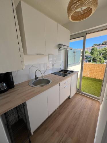 une cuisine avec des armoires blanches, un évier et une fenêtre dans l'établissement MOENA Antibes, à Antibes
