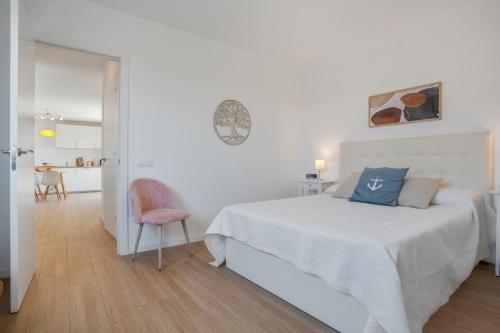 a white bedroom with a bed and a pink chair at Villa Dharma- Casa Con Encanto in La Oliva