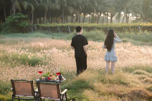 a man and a woman standing in a field with a table with wine at Nhà Yên Homestay in Kinh Dinh