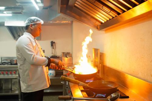 Hotel urban oasis Near Huda & Millennium City Centre Metro station I Gurgaon في جورجاون: رجل يطبخ الطعام في مقلاة ووك في المطبخ