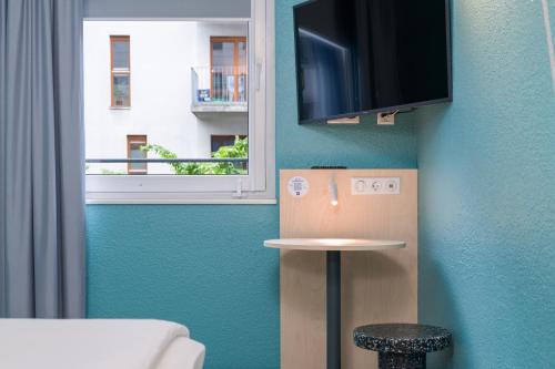 a room with a blue wall with a television and a stool at ibis budget Hamburg St Pauli Messe - neu renoviert in Hamburg