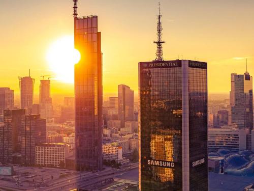 a city skyline with the sun setting behind two skyscrapers at Warsaw Presidential Hotel in Warsaw