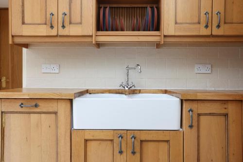 a kitchen with a white sink and wooden cabinets at JOIVY Greenknowes Farmhouse with Hot Tub and Bar in Kelty