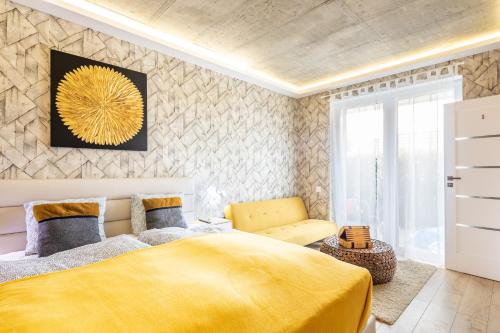 a bedroom with a yellow bed and a chair at BalatonGardens Apartman in Balatonudvari