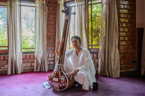 a woman sitting in a room with a guitar at SaffronStays The Divine Hima in Dharamshala