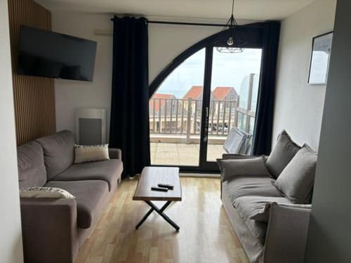 un salon avec un canapé, une table et une fenêtre dans l'établissement Appartement à la Naturelle, à Wimereux