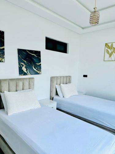 two beds in a room with white walls at 2 minutes de la plage , Résidence Tamourrit, Taghazout Bay , vue mer , golf , piscine in Taghazout