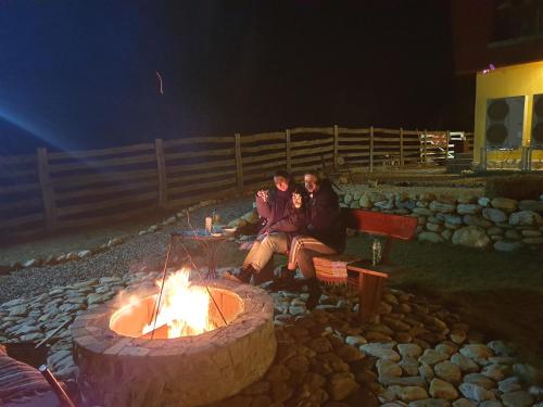 three people sitting around a fire pit at night at Pensiunea Petra Verde in Porumbacu de Sus