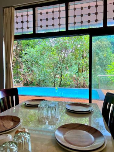 a table with plates and glasses and a large window at Nature View Villa - The Dream Stays ll Big Infinity Pool ll Wifi ll Ac ll Garden in Lonavala