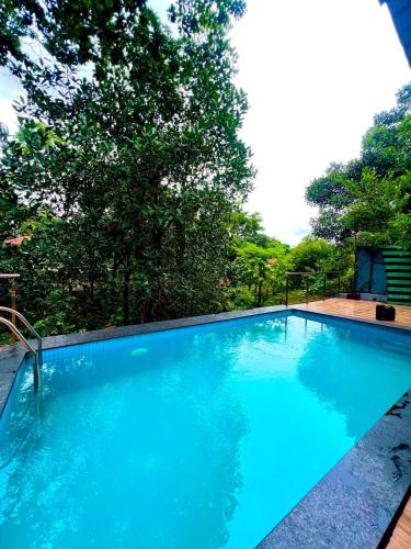 a large blue swimming pool with trees in the background at Nature View Villa - The Dream Stays ll Big Infinity Pool ll Wifi ll Ac ll Garden in Lonavala