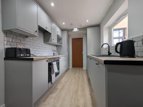 a kitchen with white cabinets and a wooden floor at Numero Uno Ensuite 3BR Flat Hot Tub Wifi Parking Contractor and Group Friendly in Birtley