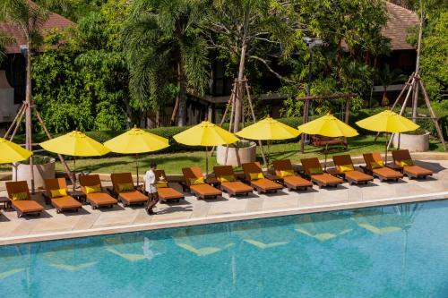 a man walking by a pool with chairs and yellow umbrellas at Pakasai Resort in Ao Nang Beach