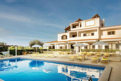 a pool in front of a building with chairs and umbrellas at Muthu Balaia Sol in Albufeira