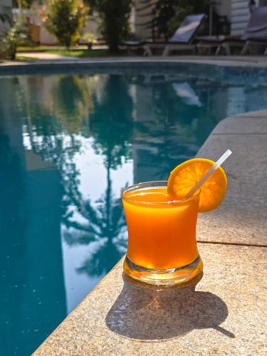 a glass of orange juice next to a swimming pool at The Verda De Miranda Resort Morjim North Goa in Morjim