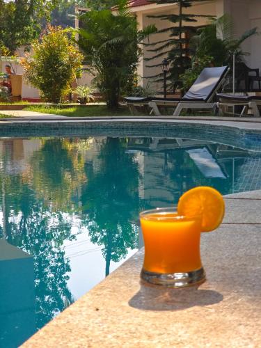 a glass of orange juice sitting next to a swimming pool at The Verda De Miranda Resort Morjim North Goa in Morjim