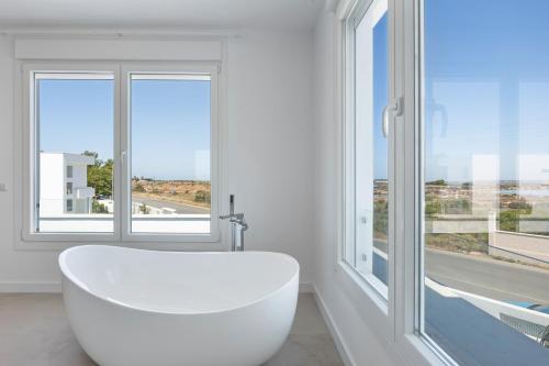 baño blanco con bañera y ventanas grandes en Villa Habana, en Poblado de Sancti Petri