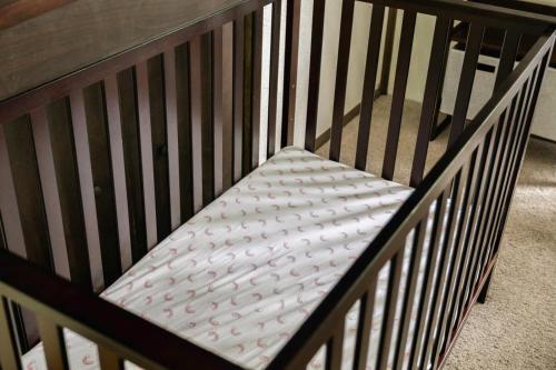 a crib with a white mattress in it at Cozy A-Frame w Fireplace Fire Pit Grill & WiFi in Hedgesville