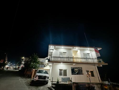 a white building with a car parked in front of it at Ganga Kinaare Homestay in Uttarkāshi