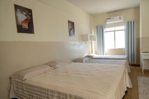 two beds in a room with a window at Hotel Centro in Corumbá