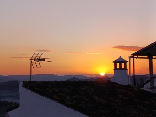 a sunset with a windmill on a hill with a lighthouse at Beautiful villa with private pool and mountain views in Jimena de la Frontera