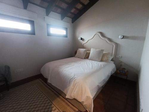 a bedroom with a white bed with two windows at Beautiful villa with private pool and mountain views in Jimena de la Frontera