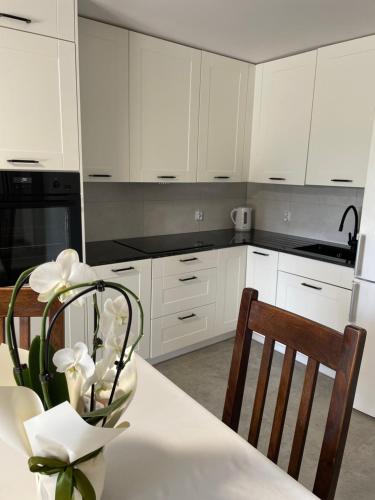 a kitchen with white cabinets and a table with flowers at Apartament Malinowe Wzgórze in Krzeszna