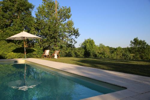 une piscine avec un parasol et deux chaises dans l'établissement La Bouchonnière, maison dans un hameau de vacances, à Monflanquin