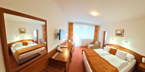 a hotel room with two beds and a mirror at Hungarospa Thermal Hotel in Hajdúszoboszló