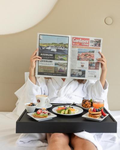 a person reading a newspaper with a tray of food at Hotel Italia in Garda